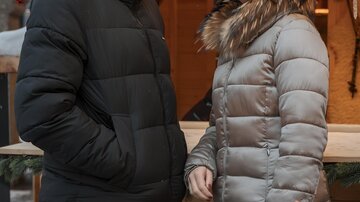 A couple is happily standing in front of a festively decorated stall. In the foreground, a cozy fire is burning.