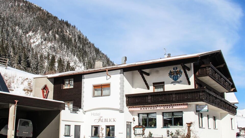 A beautiful hotel with traditional architecture in a snowy mountainous landscape. The surroundings are bordered by tall, forested mountains.