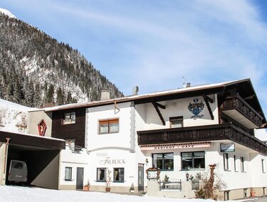 A beautiful hotel with traditional architecture in a snowy mountainous landscape. The surroundings are bordered by tall, forested mountains.