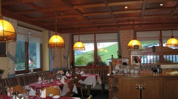 A cozy restaurant with wooden decor and warm lighting.  
Tables are elegantly set and the view outside reveals a green landscape.