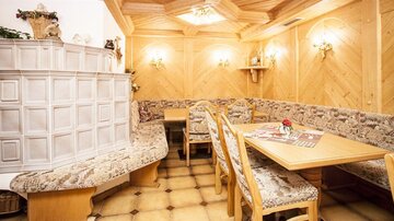 A cozy dining room with wooden paneling and a semicircular bench. Menus and a small flower arrangement are on the tables.