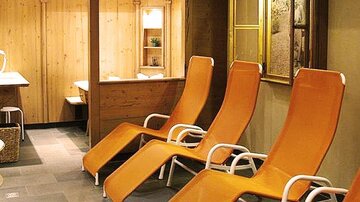 A cozy wellness area with orange loungers and wooden paneling. The room conveys a relaxing atmosphere.