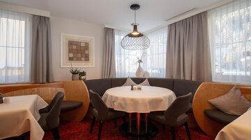 An inviting restaurant with a round table and beige chairs. Soft curtains and modern lighting create a cozy atmosphere.