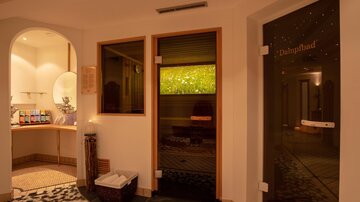 A relaxing wellness area with warm lighting and modern facilities. In the background, there is an area for treatments and a sauna.