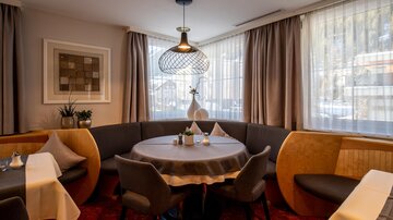 An elegant restaurant area with a round table and comfortable chairs. Large windows provide plenty of natural light and a pleasant atmosphere.