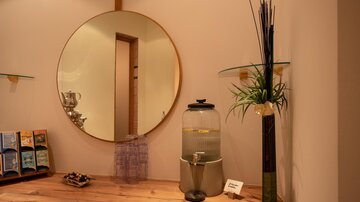 A modern reception area with a large round mirror. On the wooden shelf, there is a water station and a decorative plant.
