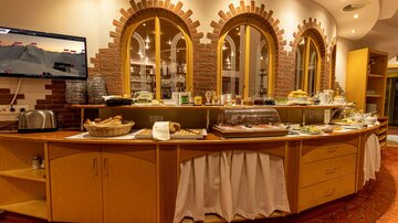 A buffet with various foods and drinks in a cozy room. Large windows with red brick arches create an inviting atmosphere.