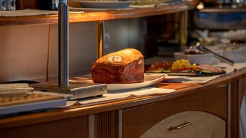 A buffet with various dishes, including a large ham on a plate. The atmosphere is bright and inviting.