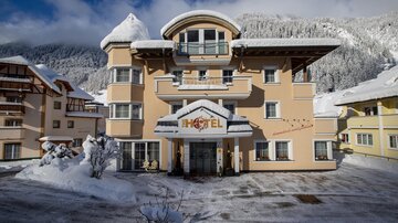 A cozy hotel in the snow, surrounded by mountains. The facade is bright with an inviting entrance area.