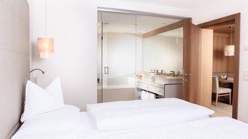 A modern hotel room with a large bed and an elegant bathroom. The space is bright and friendly designed.