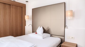 A modern bedroom with a large bed and cozy lighting. The walls are painted in neutral colors and there is a wooden wardrobe door.