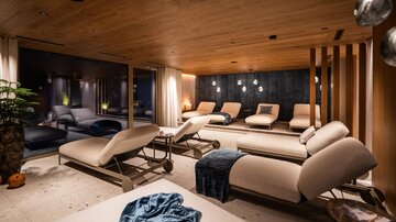 A stylish wellness room with comfortable loungers and warm wood. Soft lighting creates a relaxing atmosphere.