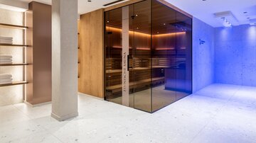 A modern sauna with a glass front and warm lights. The room is elegantly designed and offers a relaxing atmosphere.