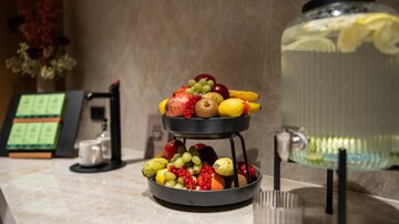 A stylish fruit platter with a selection of fresh fruits is placed on a table. Next to it, there is a pitcher of refreshing beverage.