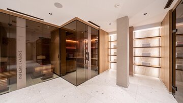 A modern space with glass walls and warm wood elements. The lighting is soft, and there are shelves for a stylish presentation.