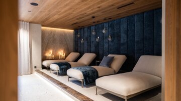 A modern relaxation room with comfortable loungers and soft lighting. The walls are mysteriously painted in dark blue, creating a calm atmosphere.