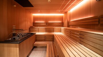 A modern wooden sauna with gentle lighting. The benches are neatly arranged, and there is a space for drinks.