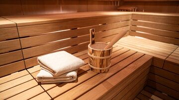 A cozy sauna with a wooden bench and a small bucket. Inside, two towels are neatly arranged.