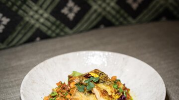 An attractively arranged plate with fried fish and colorful vegetables. The background features an elegant checkered pattern.