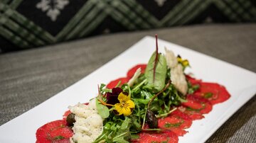 A fine dish with beef carpaccio, fresh salad, and edible flowers. The vegetables are artistically arranged on a white plate.