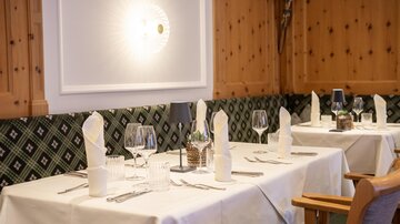 An elegant restaurant with set tables and decorative wooden elements. The tablecloths are white, and the atmosphere feels cozy and inviting.