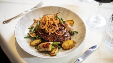 A delicious dish with fried meat, surrounded by green beans and potatoes. Accompanied by a glass of red wine.