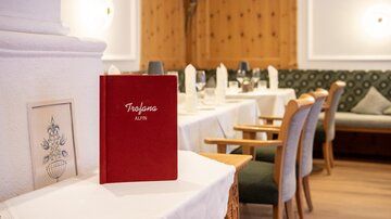 An elegant restaurant with wooden paneling and set tables. In the foreground, there is a red menu on a table.