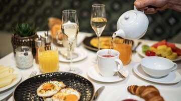 A stylish breakfast with scrambled eggs, croissants, and fresh fruit. In the background are juices and glasses for drinks.