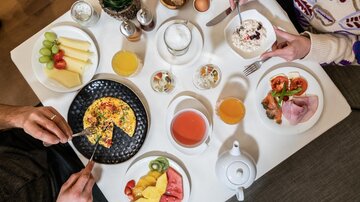 A hearty breakfast on a table with various dishes. These include an omelette, fresh fruit, cold cuts, and beverages.