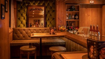 A cozy bar with wooden interior and an inviting sofa. In the background, various drinks and a Jameson advertisement can be seen.